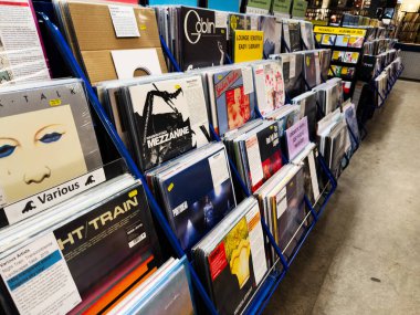 Manchester, İngiltere - 21 Ocak 2026: Mavi metal raflarında çeşitli sanatçıların yer aldığı renkli albüm kapaklarına sahip işlek bir vinil dükkanı.