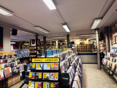 Manchester, İngiltere - 21 Ocak 2026: Parlak tepe ışıkları altında albüm rafları ve renkli kapaklarla dolu yoğun bir vinil mağazası.