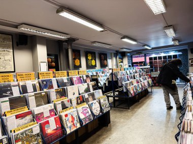 Manchester, İngiltere - 21 Ocak 2026: Parlak ışıklandırma, renkli albüm kapakları ve raflarda gezinen bir müşteri.