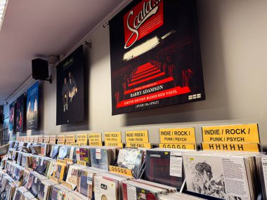 Manchester, İngiltere - 21 Ocak 2026: Sarı indie rock vinil bölümleri ve düzgün düzenlenmiş plakların üzerinde büyük bir Barry Adamson film müziği posteri olan bir plak dükkanı duvarı.