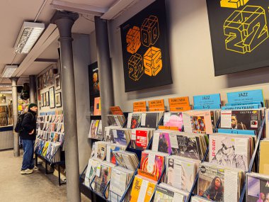 Manchester, İngiltere - 21 Ocak 2026: Gündelik alışveriş yapan kişi renkli posterler ve vitrinlerle dolu modern bir plak mağazasında plak kayıtlarına göz atıyor.