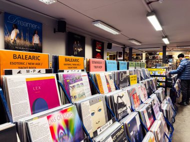 Manchester, İngiltere - 21 Ocak 2026: Parlak turuncu tabelalı canlı bir plak mağazası sahnesi, vinil rafları ve gezgin bir müşteri.