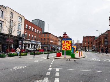 Manchester, İngiltere - 26 Ocak 2026: Parlak çiçek heykeli, tuğla binalar ve yayalarla dolu Manchester Stevenson Meydanı.