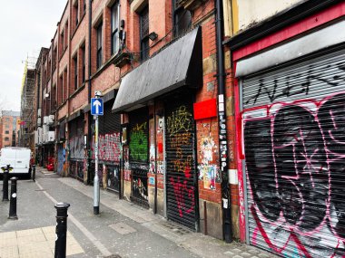 Manchester, İngiltere - 26 Ocak 2026: Manchester 'da bir sokak sahnesinde grafiti panjurlar ve tuğla mağazalar kaplıydı.