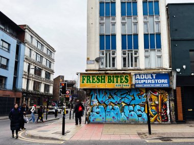 Manchester, İngiltere - 26 Ocak 2026: Manchester Oldham caddesinin köşesinde duvar resimleri, yayalar ve mağazalar bulutlu bir gökyüzü altında.