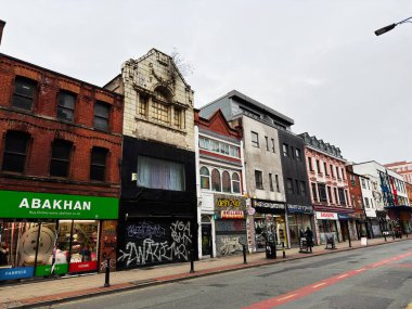 Manchester, İngiltere - 26 Ocak 2026: Manchester 'da sokak sahnesi kaldırım boyunca çeşitli mağazalar, graffiti, tuğla binalar ve yayaları gösteriyor.