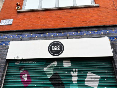 Manchester, İngiltere - 26 Ocak 2026: Manchester kentsel mağaza önü kapalı bir deklanşör duvar resmi ve Siyah Süt dairesel logosu.