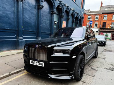 Manchester, İngiltere - 26 Ocak 2026: Parlak bir Rolls-Royce Cullinan SUV Manchester caddesi boyunca park halindeki mavi renkli bir arazi aracı.