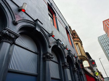 Manchester, İngiltere - 26 Ocak 2026: Manchester kentsel sokak sahnesi Wall restoran barında kemerli bant, mavi cephe ve modern şehir bloğu boyunca kırmızı ışıklar.