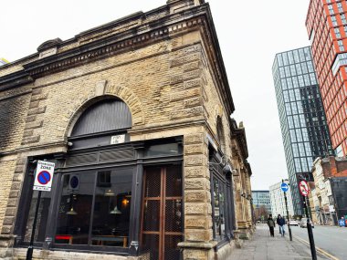 Manchester, İngiltere - 26 Ocak 2026: Eski taş mağazalar cam kulelerin yanında oturur, Manchester kentsel tarihi ve modern kontrastı yakalar.