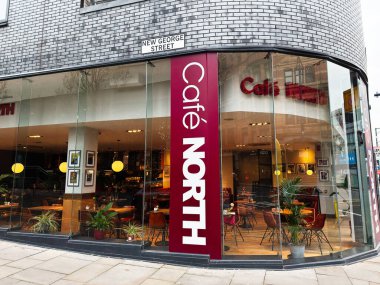 Manchester, İngiltere - 26 Ocak 2026: Manchester, İngiltere 'de cam cepheli, rahat koltuklu, bitkili ve sıcak ışıklandırmalı Modern Cafe North