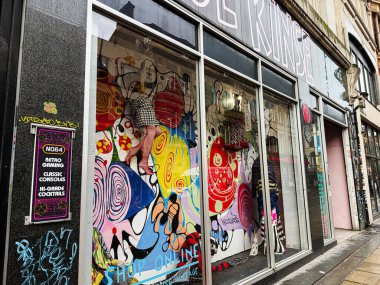 Manchester, İngiltere - 21 Ocak 2026: Manchester 'daki Vibrant NQ64 mağaza vitrininde bir duvar yazısı, moda mankenleri ve dinamik bir sokak sahnesinde retro oyun yeteneği.