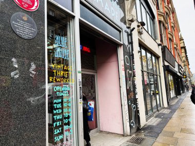 Manchester, İngiltere - 21 Ocak 2026: Manchester sokak sahnesi Blue Rinse Vintage giyim mağaza önü, grafiti, pembe kapı aralığı ve parlak açılış zamanı tabelası.