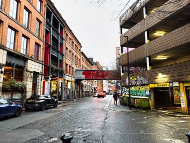 Manchester, İngiltere - 21 Ocak 2026: Moody Manchester sokak sahnesi tuğla cepheli duvar yazıları ve ıslak yol yüzeyleri.