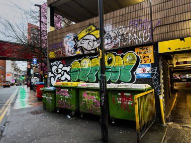 Manchester, İngiltere - 21 Ocak 2026: Duvar yazıları yağmurdan sonra Manchester caddesi boyunca yeşil çöp kutularıyla kaplandı, kentsel dayanıklılık ve renk yakaladı.