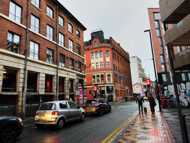 Manchester, İngiltere - 21 Ocak 2026: Manchester, İngiltere 'de Kentsel Tib Caddesi kırmızı tuğla mimari, yansıtıcı kaldırım ve hafif trafik.