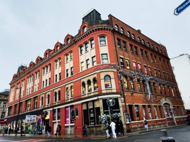 Manchester, İngiltere - 21 Ocak 2026: Meşgul Manchester caddesindeki tarihi kırmızı tuğla bina, dükkanlar, yayalar ve festival ışıkları.