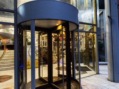 Manchester, İngiltere - 21 Ocak 2026: Manchester 'da döner kapılar, cam duvarlar ve sıcak altın ışıklı gösterişli bir otel lobisi.