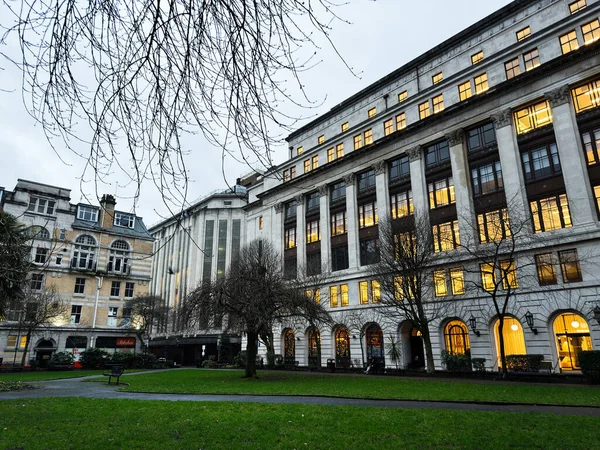 Manchester, İngiltere - 21 Ocak 2026: Manchester 'da sıcak iç ışıkları ve sessiz bir parkı olan büyük beyaz bir Arkwright House cephesinin akşam manzarası.