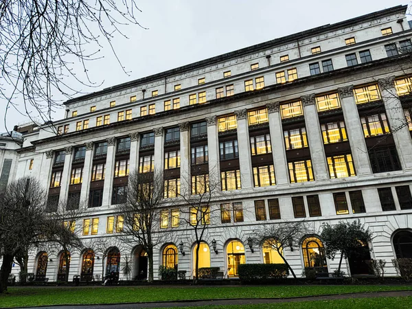 Manchester, İngiltere - 21 Ocak 2026: Parlak pencereleri ve çıplak ağaçları olan görkemli bir Arkwright House Manchester binasının akşam manzarası, neoklasik tarzda.