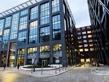 Manchester, İngiltere - 21 Ocak 2026: Manchester 'da işlek bir şehir meydanı ve yanan iç mekanları olan bir cam ofis binası.
