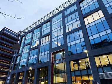 Manchester, İngiltere - 21 Ocak 2026: Büyük cam camlar, sıcak iç ışıklar ve kentsel ortam içeren One Manchester ofis cephesi.