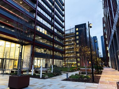 Manchester, İngiltere - 21 Ocak 2026: Manchester 'da cam ofisleri, ağaçları ve sıcak ışıklandırılmış yolları olan şehir manzarası.