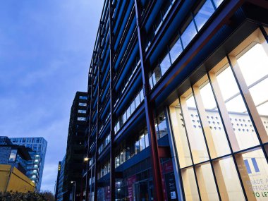 Manchester, İngiltere - 21 Ocak 2026: Manchester City 'deki akşam ışıklarını yansıtan cam paneller ve çelik çerçeveli kentsel mimari.