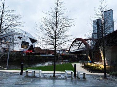 Manchester, İngiltere - 21 Ocak 2026: Manchester 'da modern mimari, yaya köprüsü ve kışın çıplak ağaçların yer aldığı nehir kenarı sahnesi. Aviva Stüdyoları, Uluslararası Fabrika 'nın evi.