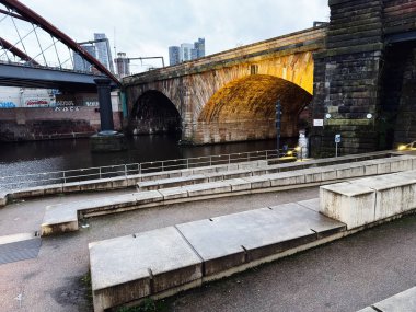 Manchester, İngiltere - 21 Ocak 2026: Manchester UK 'de şehir sahnesi uzak mesafede taş kemer köprüsü, nehir ve şehir silueti yer alıyor.