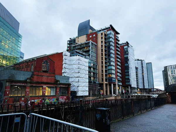 Manchester, İngiltere - 21 Ocak 2026: Manchester, İngiltere 'de bir kanal boyunca yeni cam kulelerin yanında kırmızı tuğla depo.
