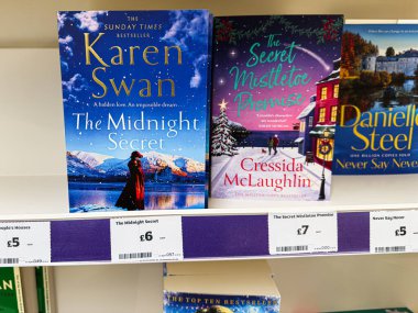 Manchester, İngiltere - 21 Ocak 2026: Rafta fiyat etiketleri ve kışlık renkli ön kapağı olan iki şenlikli aşk romanı.