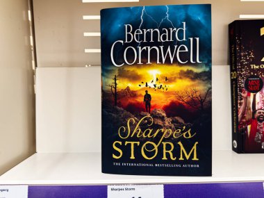 Manchester, İngiltere - 21 Ocak 2026: Kayalık arazide dramatik bir günbatımı fırtına sahnesi ve yalnız bir figürle cesur bir kitap kapağı. Bernard Cornwell, Sharpe 'ın Fırtınası.