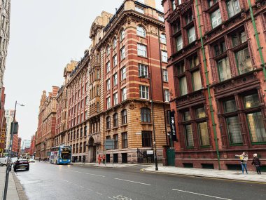 Manchester, İngiltere - 22 Ocak 2026: Manchester 'da tarihi mimari, trafik ve ıslak bir sokaktaki insanları gösteren şehir sahnesi.