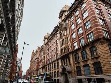 Manchester, İngiltere - 22 Ocak 2026: Manchester 'da uzun tuğla cepheler, çift katlı otobüsler ve yayalar içeren hareketli şehir caddesi.