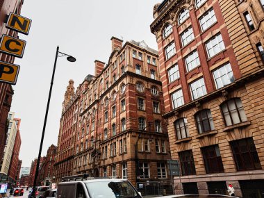 Manchester, İngiltere - 22 Ocak 2026: Kırmızı tuğlalı mimarisi, park edilmiş arabaları ve kentsel tabelaları olan yoğun bir Manchester sokak sahnesi.