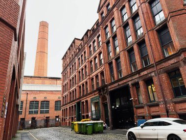 Manchester, İngiltere - 22 Ocak 2026: Manchester 'da dar bir sokak kırmızı tuğla depolarla çevrili, park edilmiş bir araba ve çöp kutularıyla.