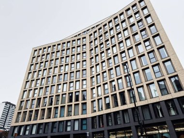 Manchester, İngiltere - 22 Ocak 2026: İngiltere 'deki modern eğri büğrü Manchester Meydanı ön cephe ofis binası, cam pencereli ve sokak ışıklandırmalı kentsel manzara.