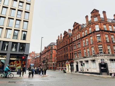 Manchester, İngiltere - 22 Ocak 2026: Manchester 'da yayalar, bisikletçiler ve tarihi kırmızı tuğla mimari ile kentsel sokak sahnesi.