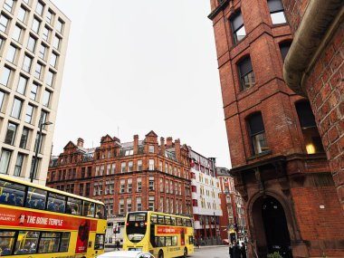 Manchester, İngiltere - 22 Ocak 2026: Kırmızı tuğla mimari ikonik sarı otobüsler ve kentsel yaşamla dolu kalabalık bir Manchester caddesini çiziyor.