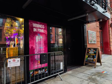 Manchester, İngiltere - 22 Ocak 2026: Parlak pembe içecek afişi ve kentsel mağaza vitrinli renkli Manchester sokak sahnesi.