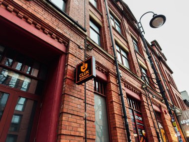 Manchester, İngiltere - 22 Ocak 2026: Kırmızı tuğla bina, neon ışıklı kulüp tabelası, sokak lambası ve Manchester UK şehir merkezindeki kentsel mağazalar.