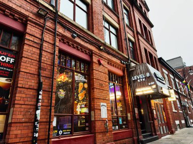 Manchester, İngiltere - 22 Ocak 2026: Canlı bir Manchester caddesi kırmızı tuğlalı binalar, neon seviye 8 KTV tabelaları ve parlak bir mekan önü.