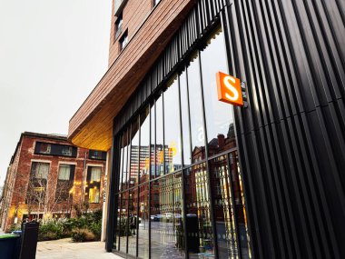 Manchester, İngiltere - 22 Ocak 2026: Sainsbury 'nin Manchester mağazası cam cepheli ve bir şehir caddesi boyunca belirgin turuncu S işareti.