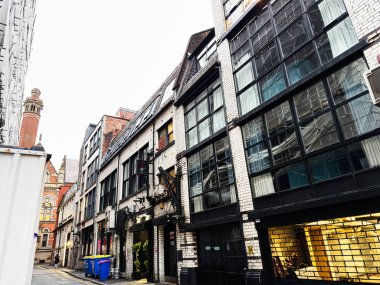 Manchester, İngiltere - 22 Ocak 2026: Manchester 'da dar bir şerit, tuğla ve cam binalar ve parlak vitrinlerle kentsel sokak sahnesi.