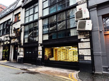 Manchester, İngiltere - 22 Ocak 2026: Günümüz modern cam cephe, siyah çerçeve ve sıcak iç aydınlatma ve kentsel atmosfer içeren şehir sokak sahnesi.