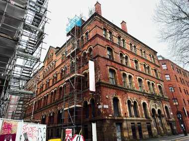 Manchester, İngiltere - 22 Ocak 2026: Manchester 'daki kırmızı tuğla bina iskelesi, inşaat çalışması, kentsel sokak sahnesi ve tarihi mimari.