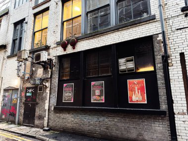 Manchester, İngiltere - 22 Ocak 2026: Tuğla duvarlı, ışıklı pencereli, kadife bar posterli ve kentsel karamsar atmosferli Gritty Manchester sokak sahnesi.