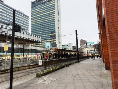 Manchester, İngiltere - 22 Ocak 2026: İnsanlar Manchester Piccadilly Gardens 'ta uzun ofis bloklarının yanındaki tramvay durağında bekliyor..