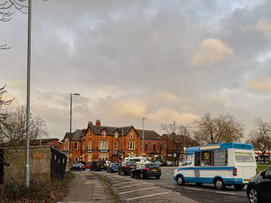 Manchester, İngiltere - 23 Ocak 2026: Manchester 'da kırmızı tuğlalı evler, park edilmiş arabalar ve yol kenarında mavi bir dondurma kamyoneti bulunan işlek bir sokak.